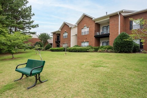 a park bench sits in the grass in front of an apartment building